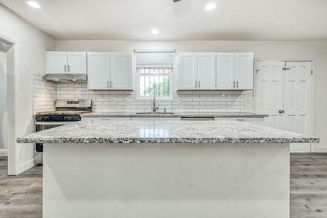 kitchen featuring light stone counters, white cabinets, stainless steel gas stove, a center island, and light hardwood / wood-style floors