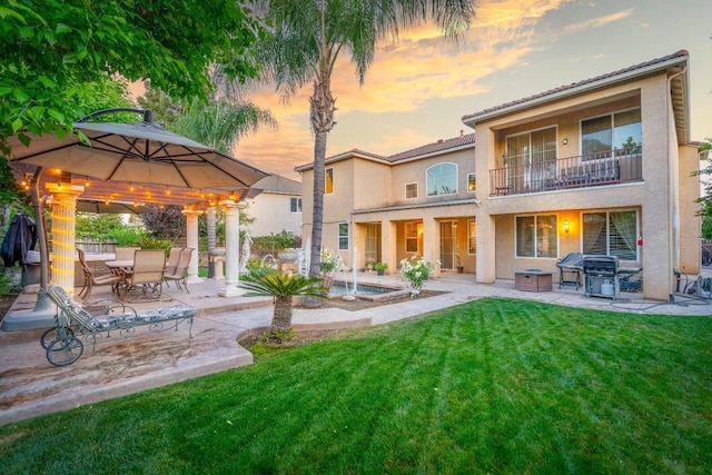 back house at dusk featuring a balcony, a gazebo, a lawn, and a patio area