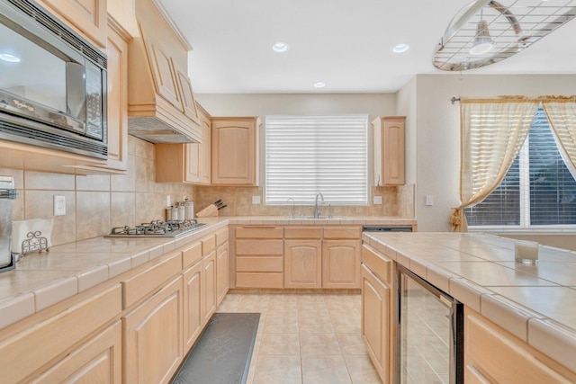 kitchen featuring black microwave, light brown cabinets, wine cooler, stainless steel gas stovetop, and tile countertops