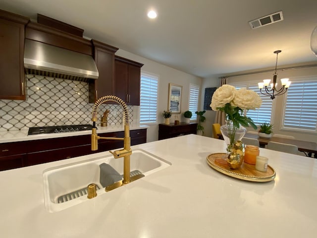 kitchen with sink, wall chimney exhaust hood, gas cooktop, decorative light fixtures, and decorative backsplash