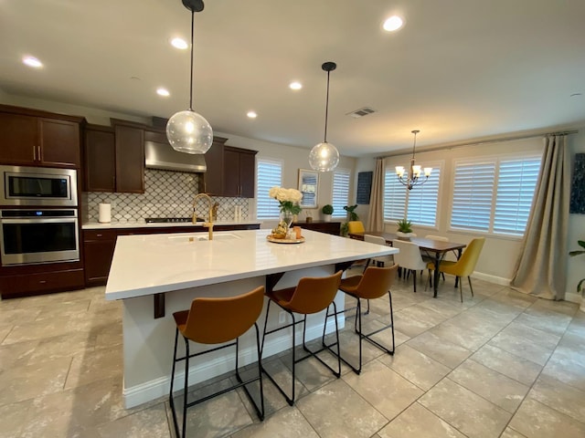 kitchen with sink, wall chimney exhaust hood, tasteful backsplash, an island with sink, and appliances with stainless steel finishes