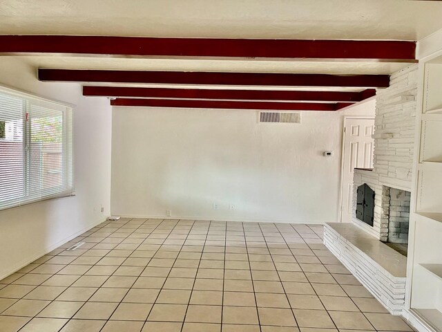 unfurnished living room featuring beamed ceiling, light tile patterned floors, and a fireplace