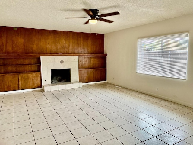 unfurnished living room featuring wooden walls, ceiling fan, light tile patterned floors, a textured ceiling, and a tiled fireplace