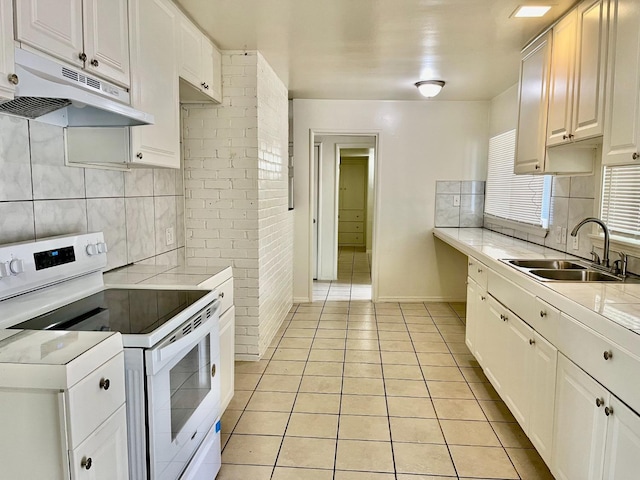 kitchen with white electric range oven, light tile patterned floors, white cabinetry, and sink