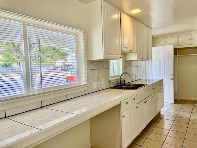 kitchen with decorative backsplash, sink, light tile patterned floors, white cabinets, and tile counters