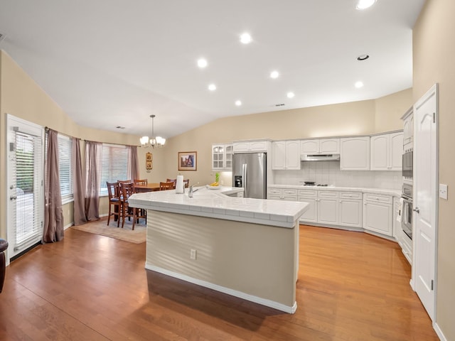 kitchen with hanging light fixtures, stainless steel appliances, vaulted ceiling, light wood-type flooring, and white cabinetry