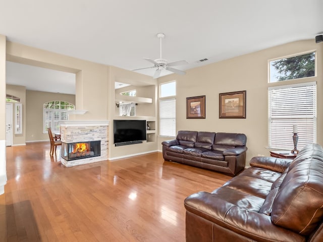 living room featuring ceiling fan, a stone fireplace, and light hardwood / wood-style flooring