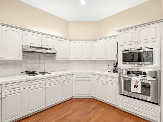 kitchen with tile countertops, backsplash, white cabinetry, light hardwood / wood-style floors, and stainless steel appliances