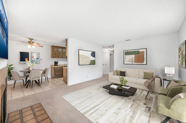 living room with light carpet, ceiling fan, and a textured ceiling