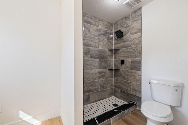 bathroom with a tile shower, a textured ceiling, toilet, and wood-type flooring