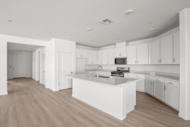 kitchen featuring white cabinets, an island with sink, light hardwood / wood-style floors, stainless steel range with gas cooktop, and sink