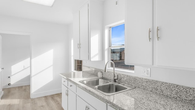 kitchen featuring light stone counters, light wood-type flooring, sink, and white cabinetry