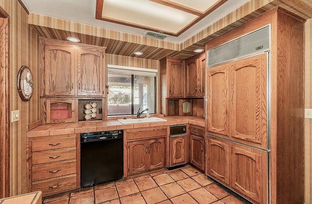 kitchen with tile counters, wood walls, black dishwasher, and sink