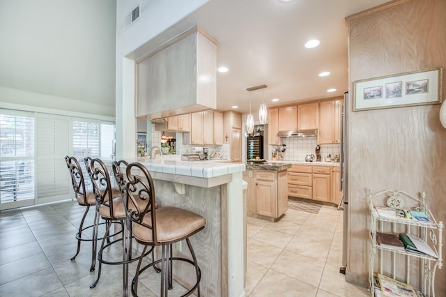 kitchen with a kitchen island, light brown cabinets, light tile patterned flooring, kitchen peninsula, and hanging light fixtures