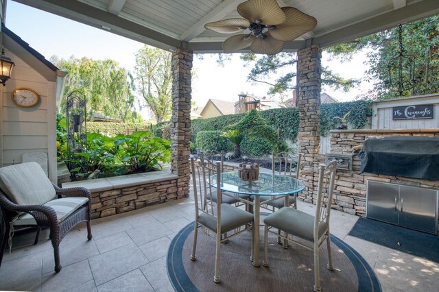 view of patio with a ceiling fan, grilling area, outdoor dining space, fence, and an outdoor kitchen