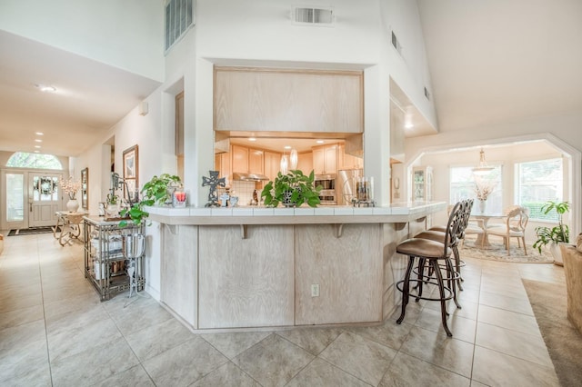 kitchen with a kitchen breakfast bar, light brown cabinets, tile countertops, kitchen peninsula, and high vaulted ceiling