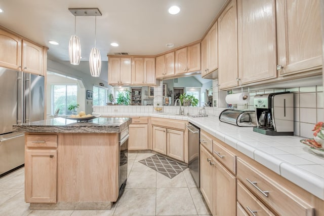 kitchen with light brown cabinets, light tile patterned floors, sink, a kitchen island, and stainless steel appliances