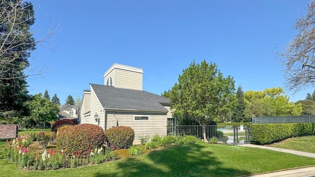 view of side of home with a shingled roof, fence, and a lawn