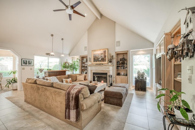 living area featuring high vaulted ceiling, a ceiling fan, a glass covered fireplace, light tile patterned flooring, and beam ceiling