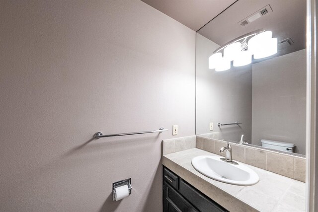 bathroom with toilet, vanity, and visible vents