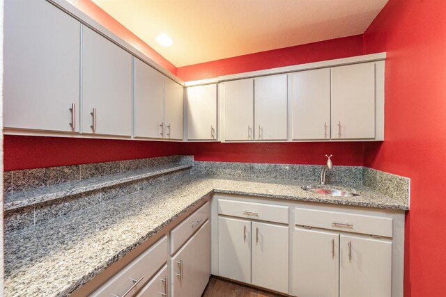kitchen featuring white cabinetry, a sink, and light stone countertops