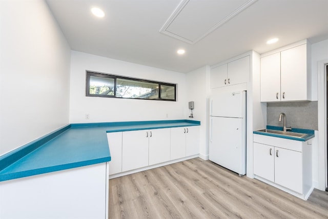 kitchen featuring sink, light hardwood / wood-style flooring, backsplash, white fridge, and white cabinets