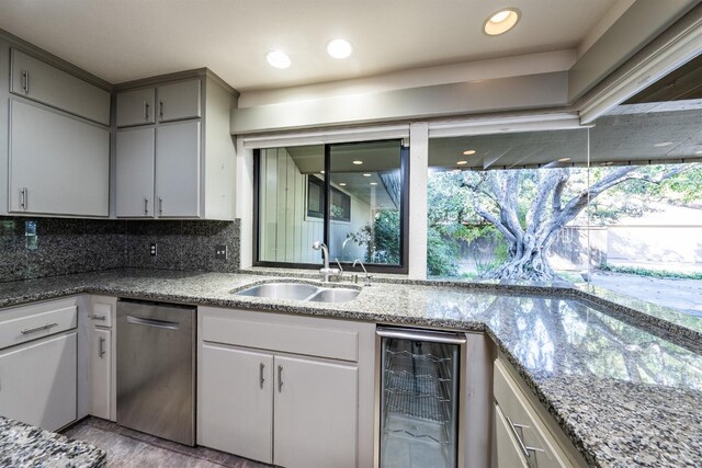 kitchen with tasteful backsplash, stainless steel dishwasher, a sink, light stone counters, and beverage cooler