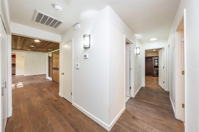 hallway featuring dark wood finished floors, baseboards, and visible vents