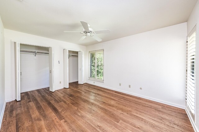unfurnished bedroom with baseboards, wood finished floors, two closets, and ceiling fan