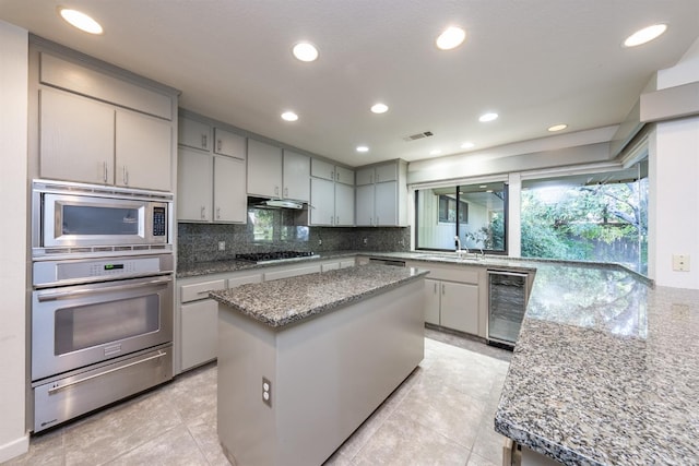 kitchen with light stone countertops, appliances with stainless steel finishes, a center island, gray cabinets, and wine cooler