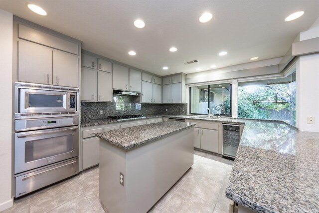 kitchen featuring tasteful backsplash, appliances with stainless steel finishes, under cabinet range hood, beverage cooler, and a warming drawer