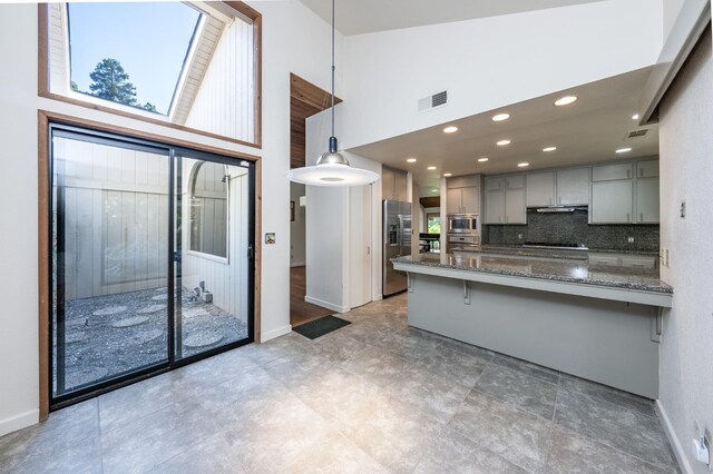kitchen with high vaulted ceiling, a peninsula, stainless steel appliances, gray cabinetry, and a kitchen breakfast bar
