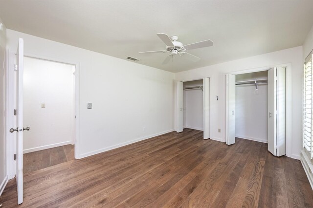 unfurnished bedroom featuring a ceiling fan, baseboards, visible vents, two closets, and dark wood-type flooring