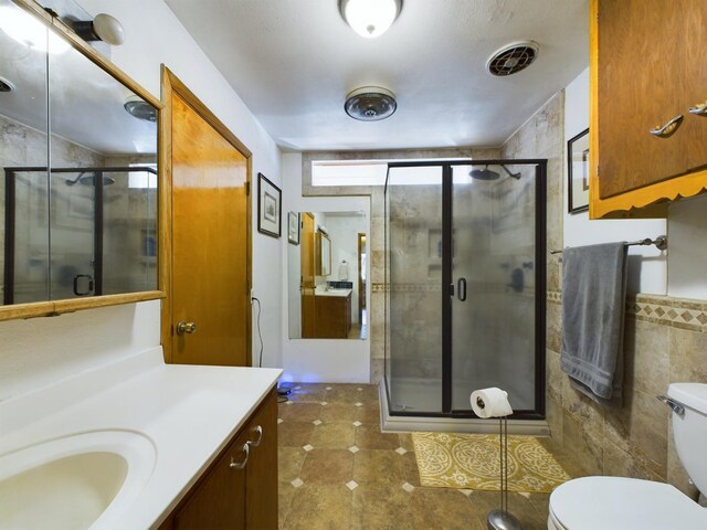 bathroom with vanity, tile walls, a shower with shower door, and toilet