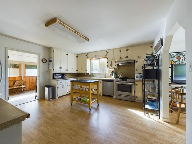 kitchen with stainless steel appliances, light hardwood / wood-style floors, white cabinets, and tasteful backsplash