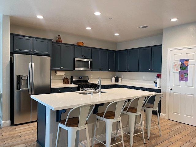 kitchen featuring stainless steel appliances, a center island with sink, light wood-type flooring, and a breakfast bar