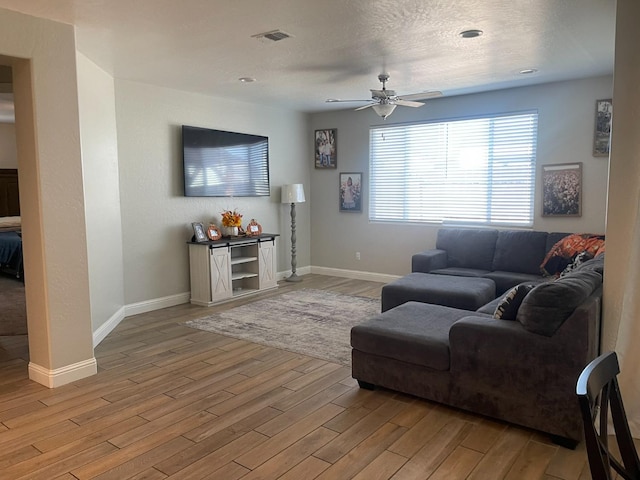 living room featuring ceiling fan, a textured ceiling, and light wood-type flooring