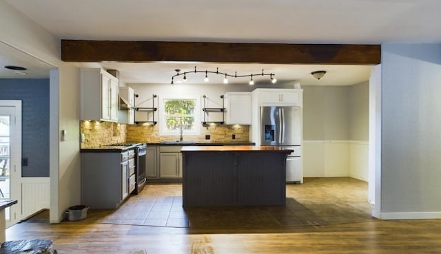 kitchen with appliances with stainless steel finishes, beamed ceiling, a center island, and light hardwood / wood-style floors