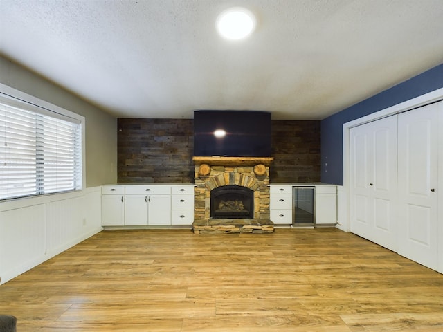 unfurnished living room with light wood-type flooring, wine cooler, a stone fireplace, and a textured ceiling