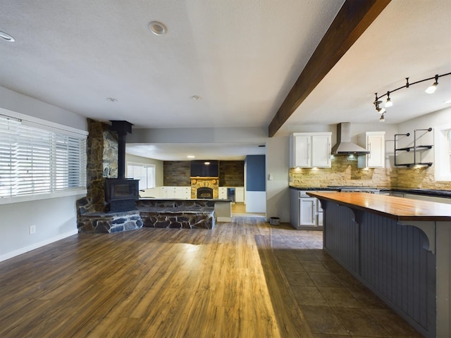 kitchen with wall chimney range hood, beamed ceiling, butcher block counters, dark hardwood / wood-style floors, and white cabinets