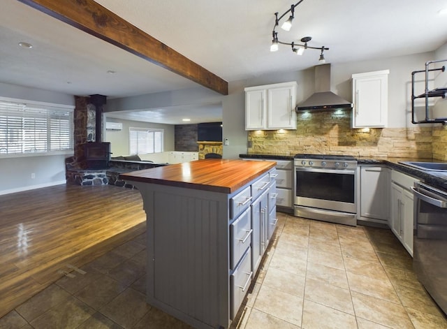 kitchen featuring a wood stove, a healthy amount of sunlight, wall chimney range hood, and stainless steel appliances