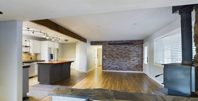 kitchen with hardwood / wood-style floors, brick wall, stainless steel appliances, white cabinets, and a center island