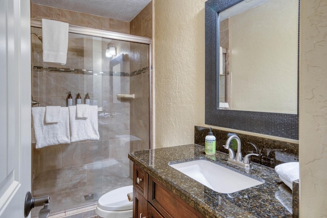 bathroom featuring vanity, a shower with shower door, toilet, and a textured ceiling