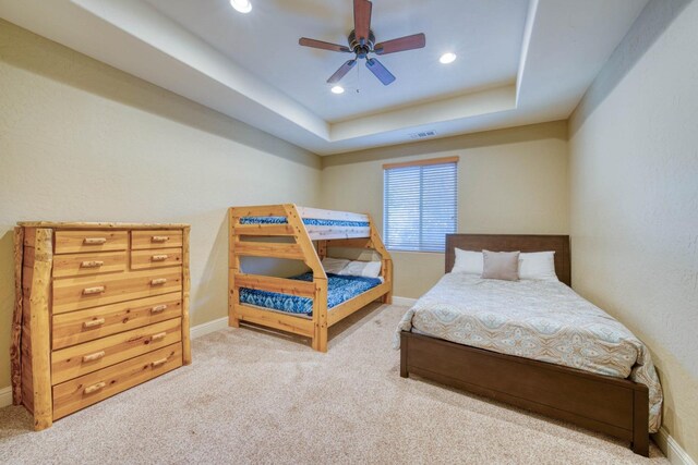 carpeted bedroom featuring ceiling fan and a tray ceiling