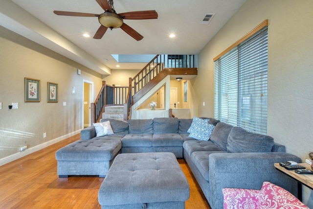 living room with a skylight, ceiling fan, and light hardwood / wood-style floors