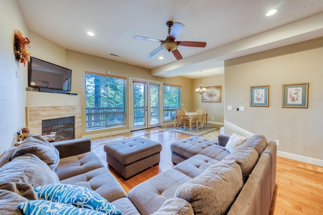 living room with ceiling fan with notable chandelier, a fireplace, and light hardwood / wood-style flooring