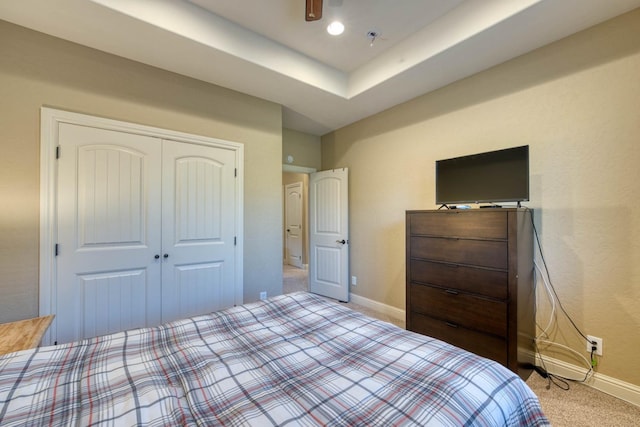 carpeted bedroom featuring ceiling fan, a closet, and a raised ceiling