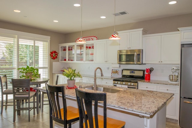 kitchen featuring white cabinets, sink, decorative light fixtures, a kitchen island with sink, and stainless steel appliances