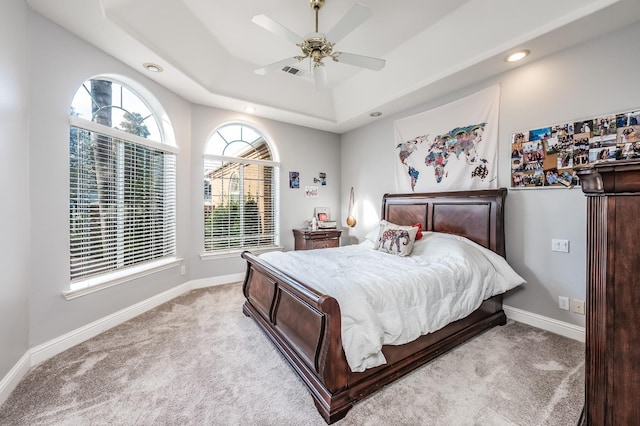 bedroom with light carpet, ceiling fan, and a tray ceiling