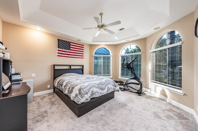 bedroom with light colored carpet, ceiling fan, and a tray ceiling